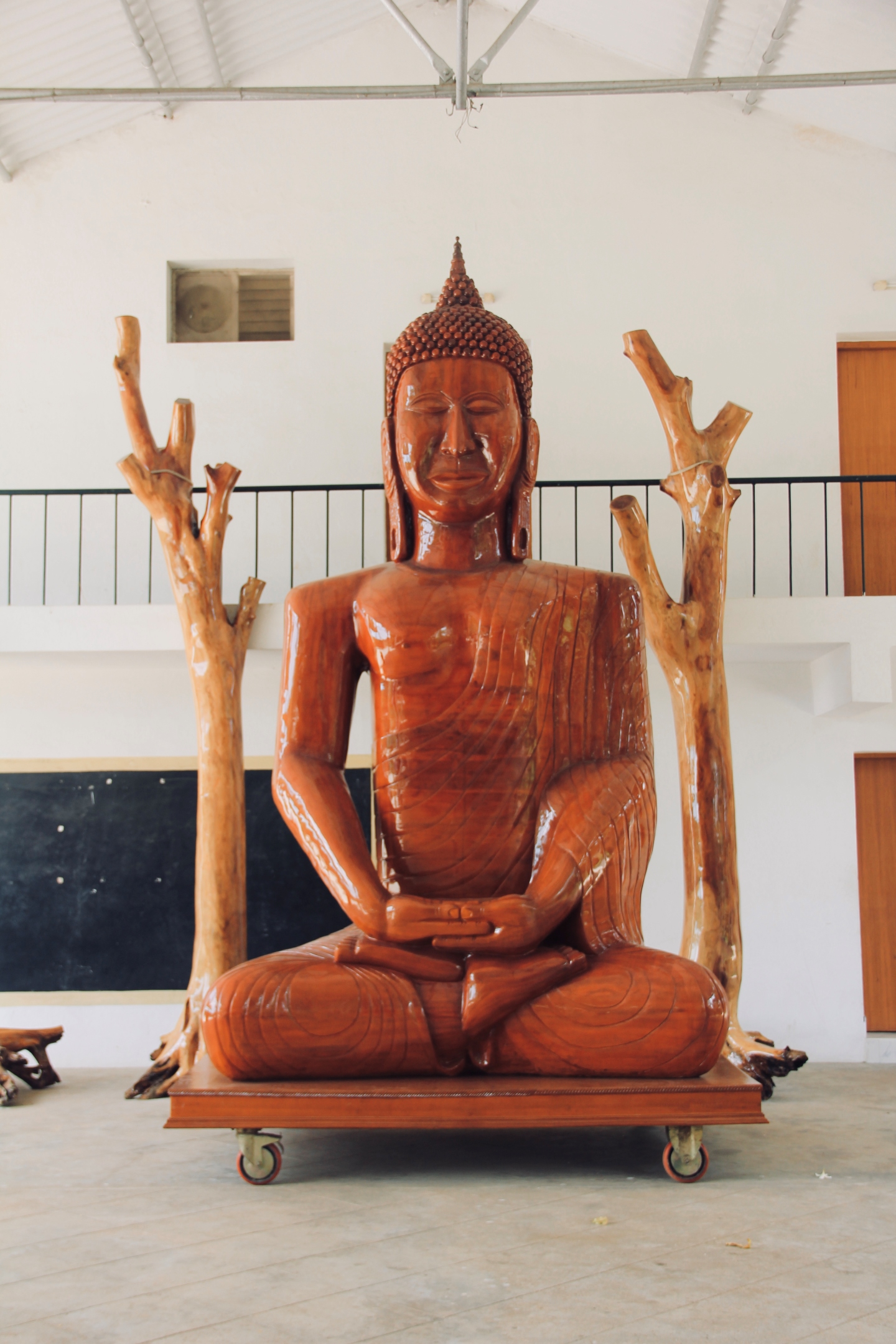 Unfinished wooden Buddha sculpture with raised branch-like arms, in progress at the studio