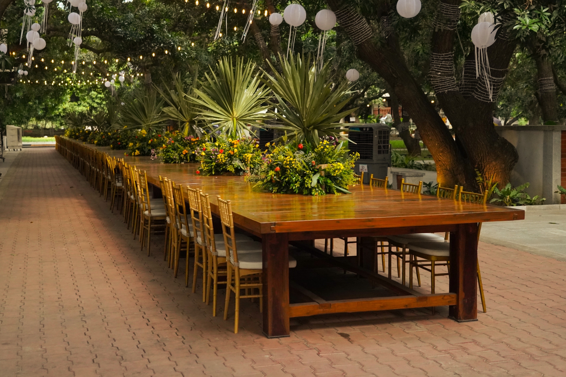 Long banquet table crafted from reclaimed wood, set under trees with fairy lights